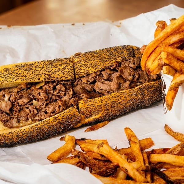 A cheesesteak sandwich on a poppy seed roll with a side of golden french fries.